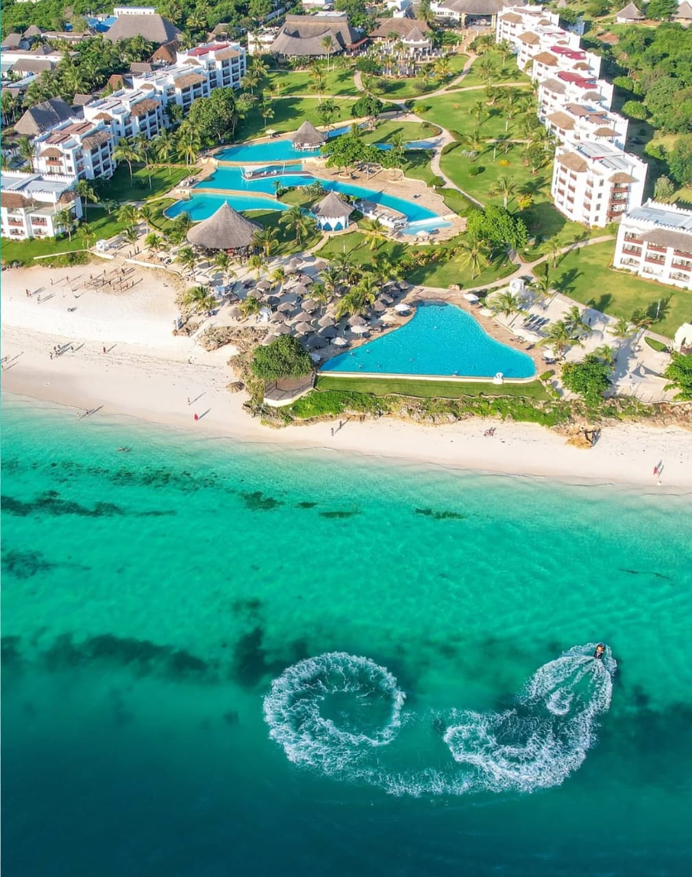 Aerial view of a Zanzibar beach resort, turquoise pools and a jet ski circling offshore